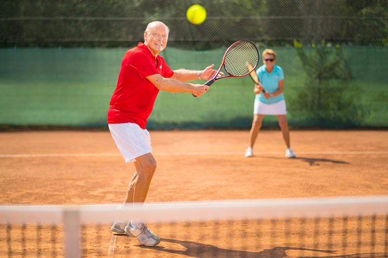 Older adults play tennis on a clay court, as part of their strategy to stay healthy and fit