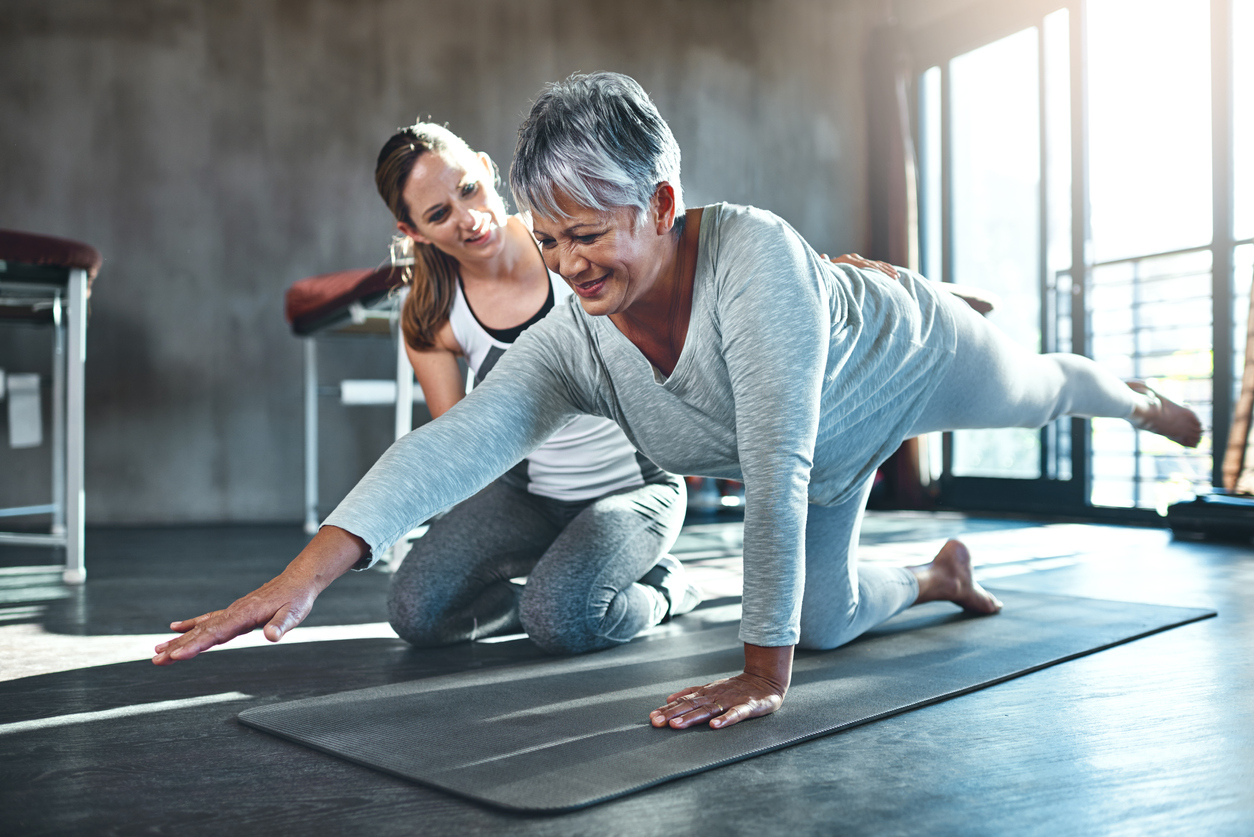 Older woman exercises with a personal trainer at her 55+ community’s fitness center