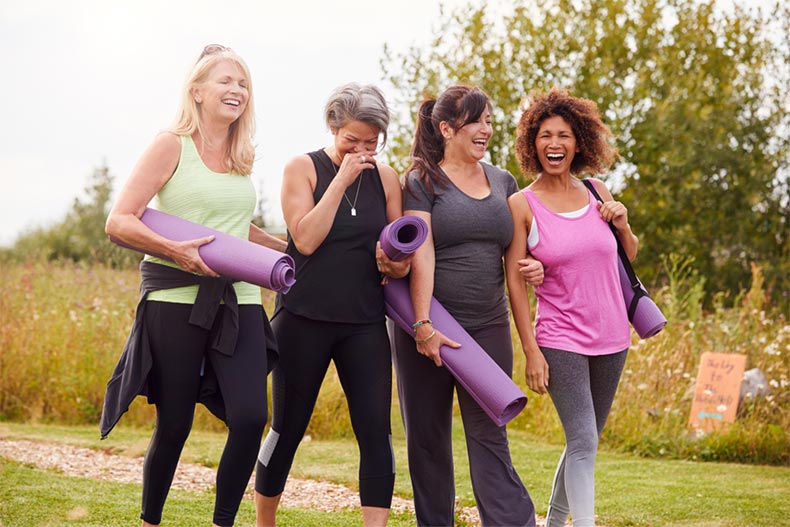 A group of older female friends walking along a path with yoga mats