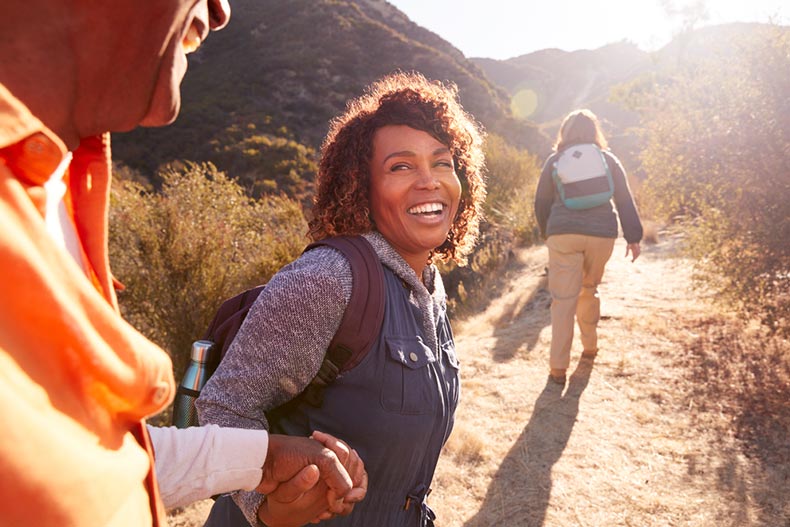 An older woman holding her partner's hand as they head down a nature trail with a hiking group