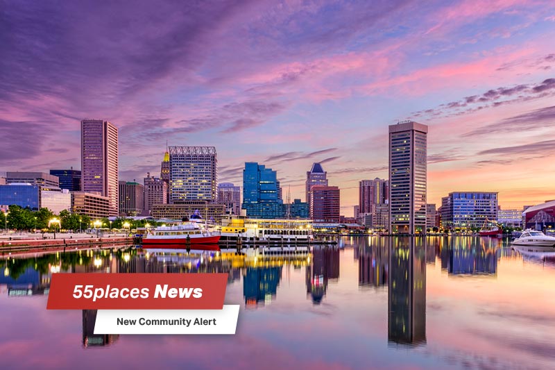 Baltimore, MD skyline at the Inner Harbor at dusk with 55places News banner overlay and new community alert text.
