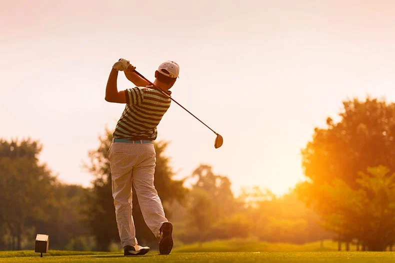 Photo of a golfer swinging his club toward the sunset