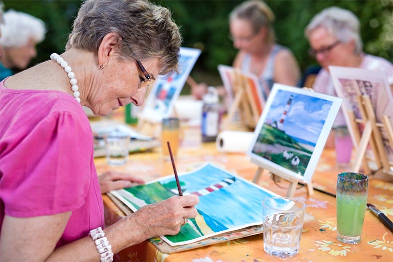 A group of senior women creating watercolor paintings at a table outside