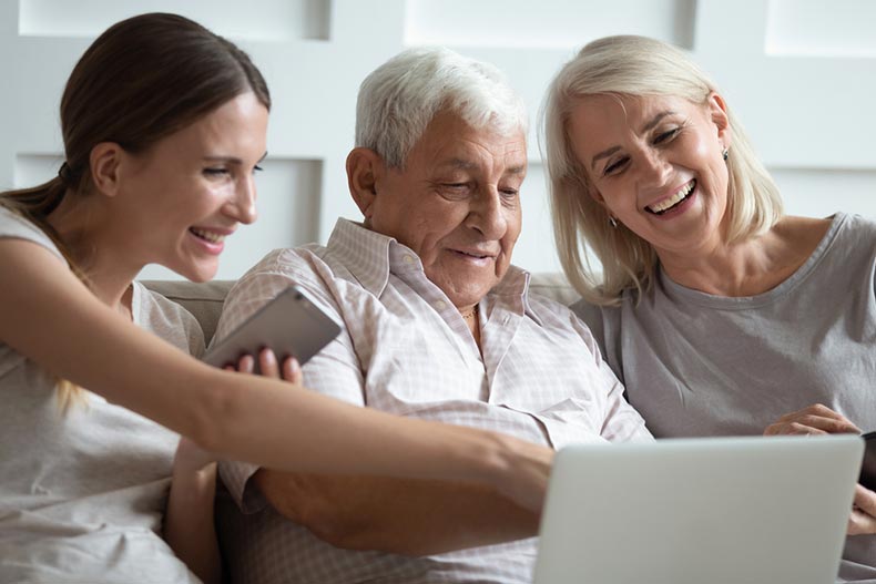 A grownup daughter helping her parents use a laptop to search for 55+ communities