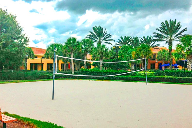 A beach volleyball court in front of palm trees and a yellow amenity center, located in the Pelican Preserve community of Fort Myers, Florida