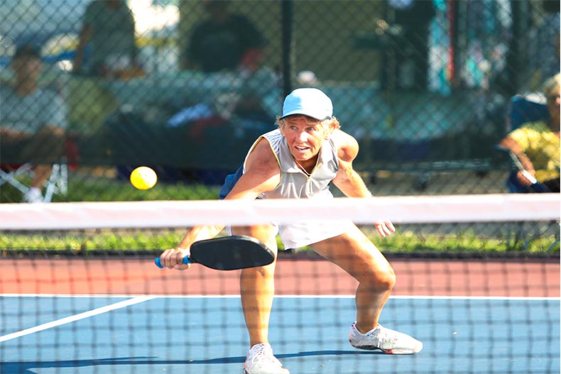Women leaning forwards to hit a pickleball
