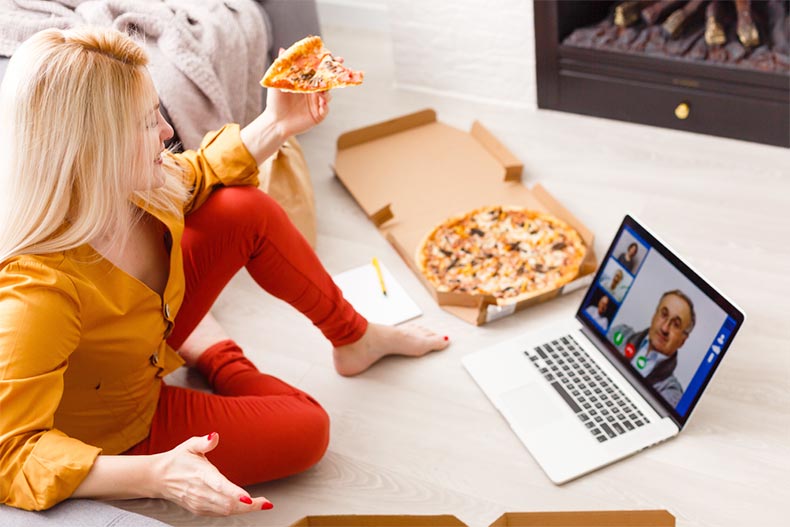 A woman sitting on the floor and eating pizza while video chatting