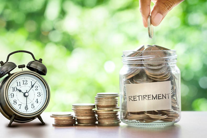 A hand dropping a coin in a jar labeled "retirement" beside an alarm clock