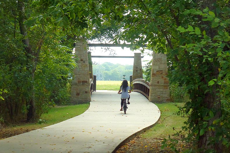 View of a person riding a bike on a pathway framed by trees in Oak Point Nature Preserve in Plano, Texas