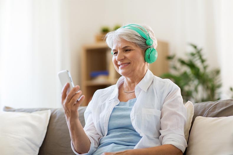 A senior woman with green headphones sitting on a couch and listening to her favorite podcast