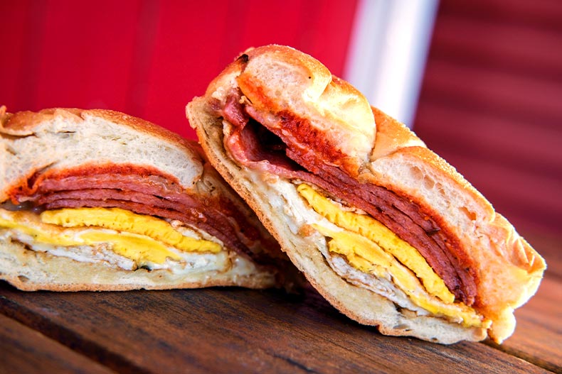 A pork roll, egg, and cheese breakfast sandwich on a kaiser roll located on a wooden picnic table