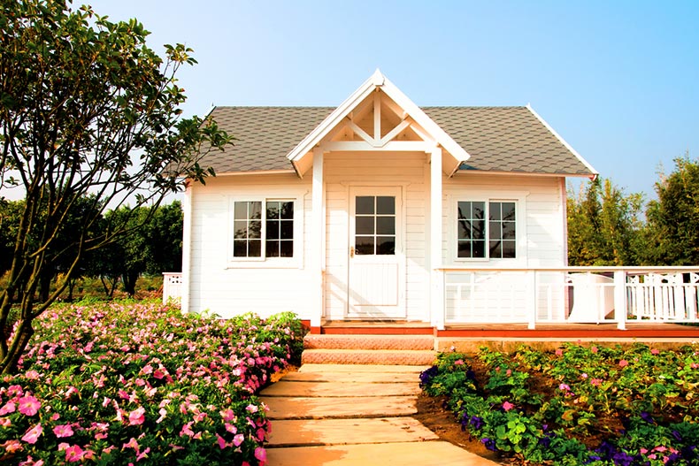 A small, white house surrounded by flowers in the countryside