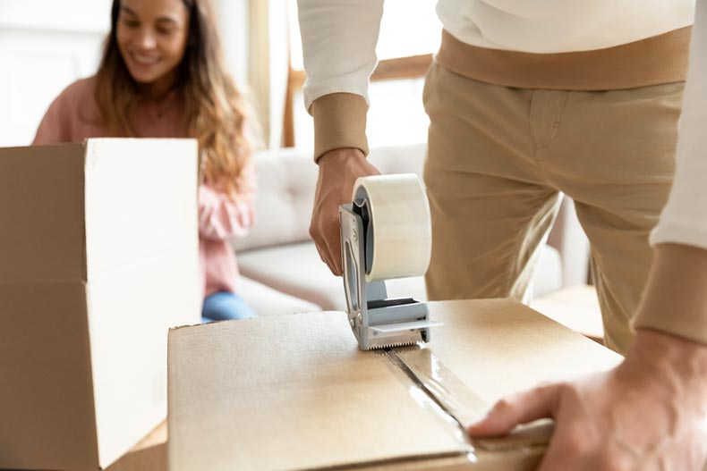A man holding a tape dispenser while packing a cardboard box on moving day