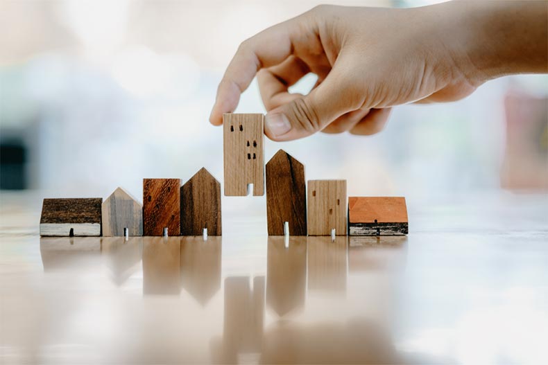A hand placing mini wood house models in a row on a wood table