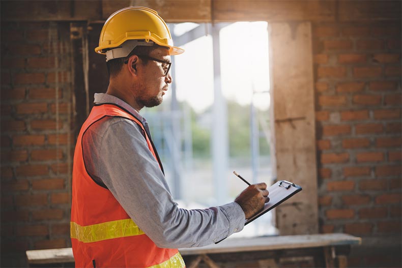 A home inspector checking a property and taking notes on a clipboard