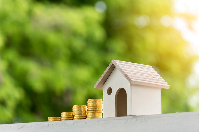 A small wooden house beside a stack of gold coins