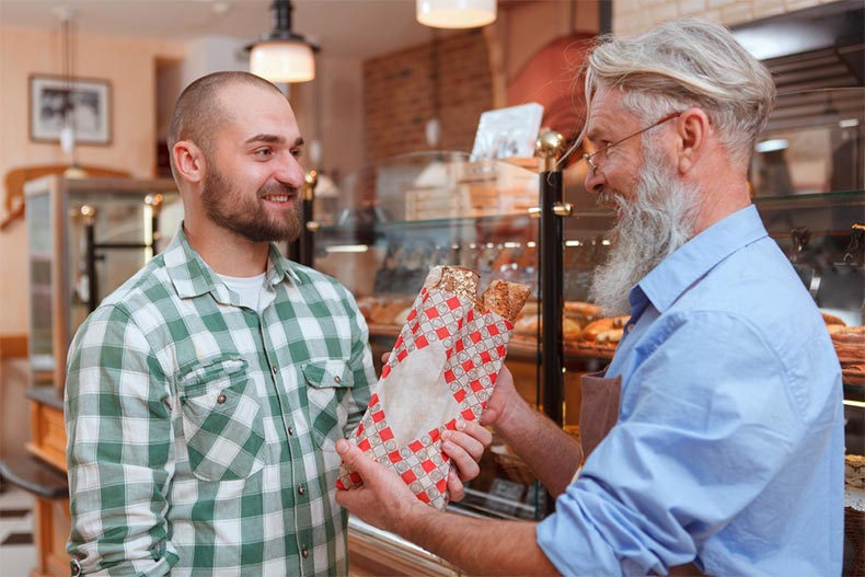 A senior man selling fresh bread to a customer in a bakery