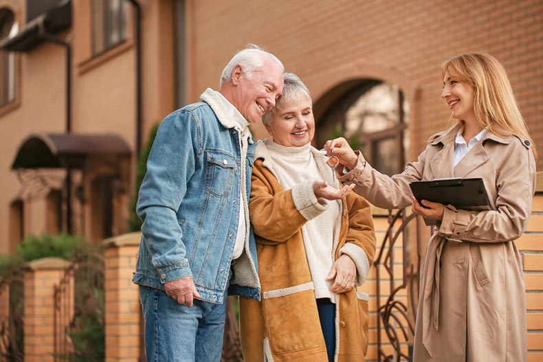 A real estate agent handing a senior couple the keys to their new home