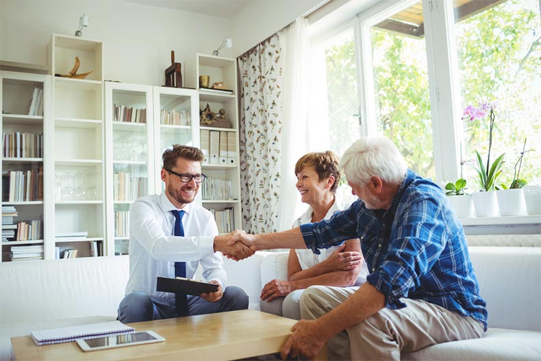 A real estate agent shaking hands with an active adult couple in a living room
