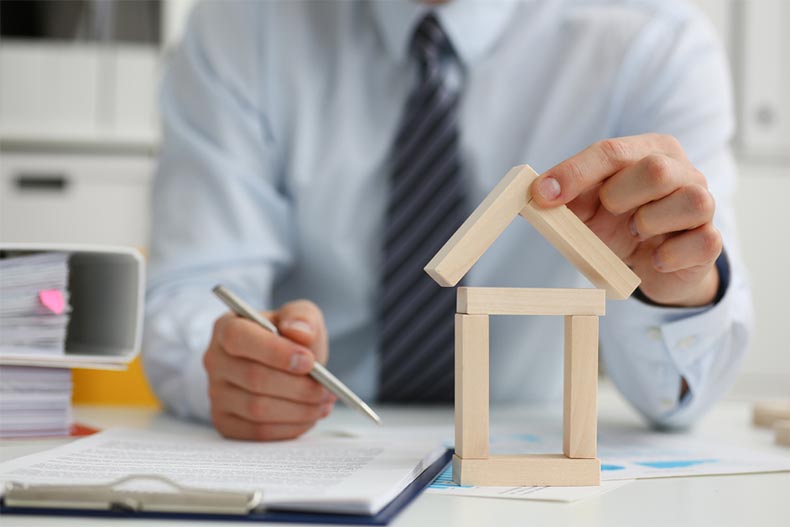 Male hands signing a document on a clipboard while placing some blocks to form a house outline