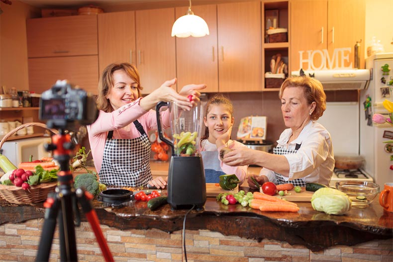 Two women and young girl recording themselves making food in a kitchen.