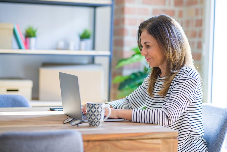 A senior woman sitting at a table at home and using a laptop to search for volunteer opportunities