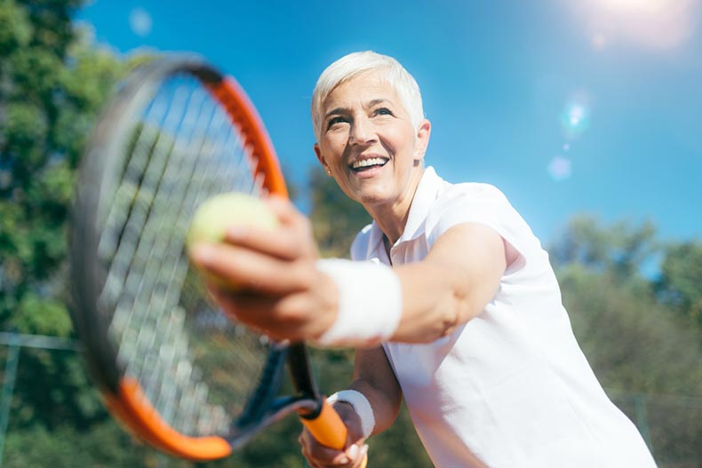 An older woman smiling while playing tennis on a sunny day in her 55+ community