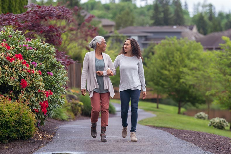 A younger woman walks along a path with an older woman in a 55+ community
