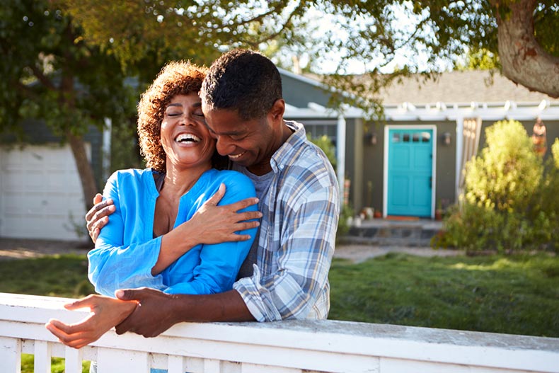 An older couple laughing and leaning on the fence outside their new home