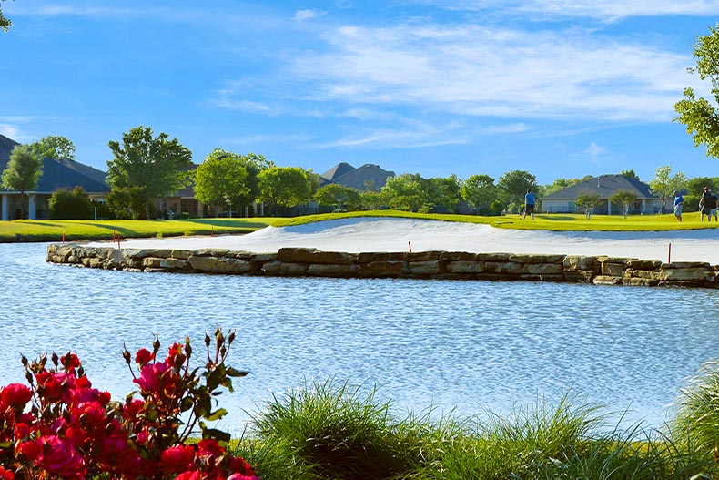 View of a bunker beyond a pond and several red flowers in Robson Ranch, Eloy, Arizona