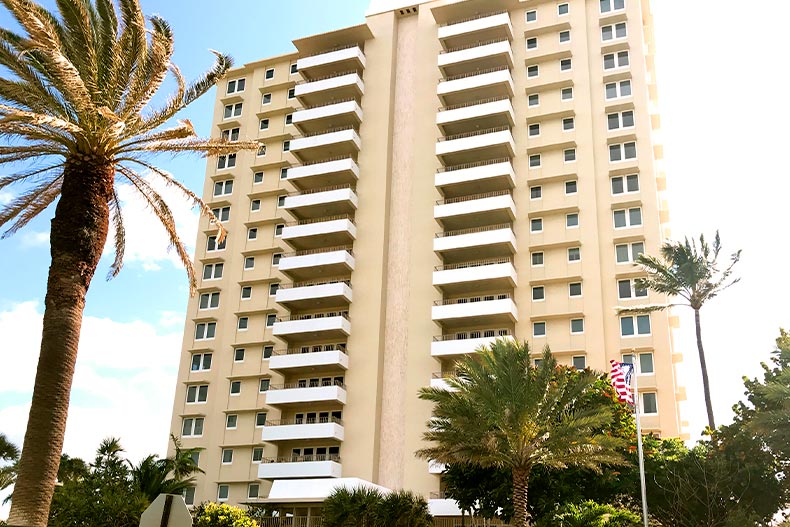 Exterior view of the tall Sabal Ridge condominium complex surrounded by palm trees on a sunny day, located in Boca Raton, Florida