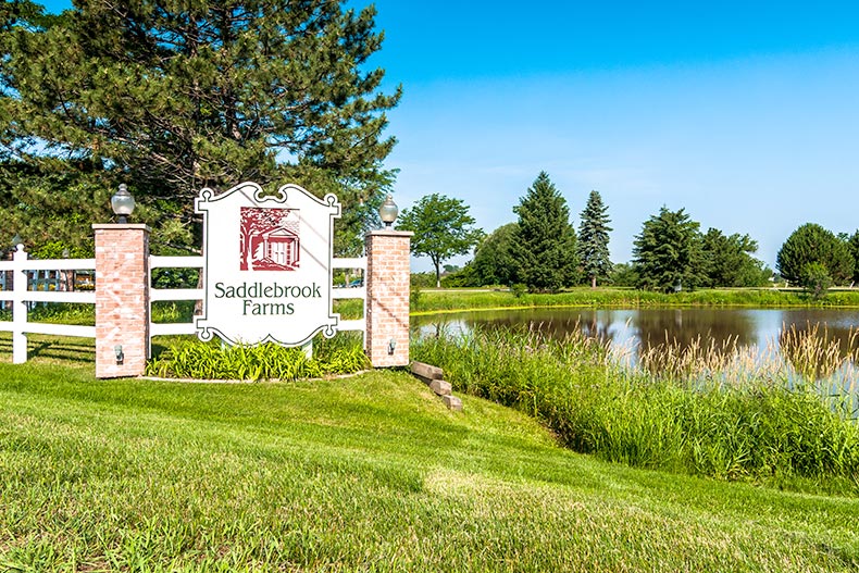 Greenery and a pond beside the community sign for Saddlebrook Farms in Grayslake, Illinois