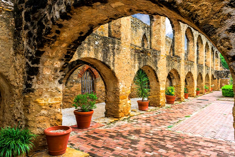 Interior view of a courtyard with potted plants placed in archways, located in the San Jose Mission of San Antonio, Texas