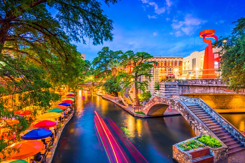 Overhead view of the San Antonio, Texas River Walk at sunset with colorful umbrellas lining the river and boat speed lines above the water