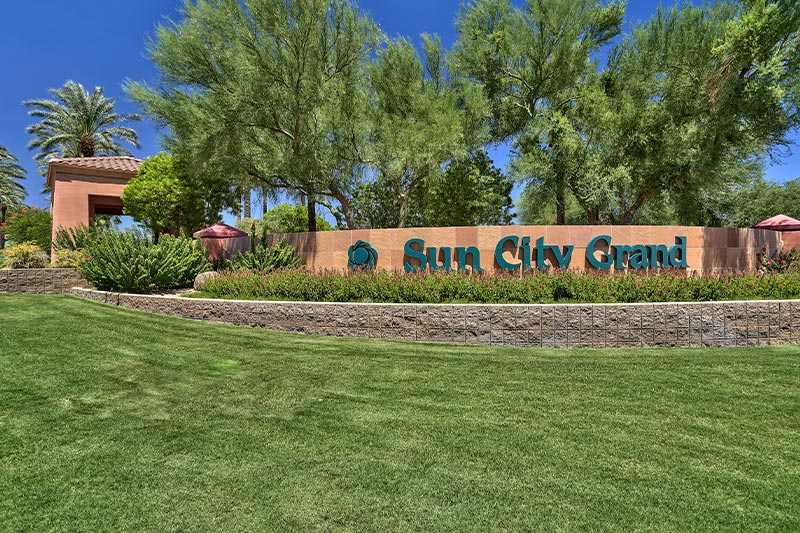 View of the community sign at Sun City Grand with lush tress in the background.