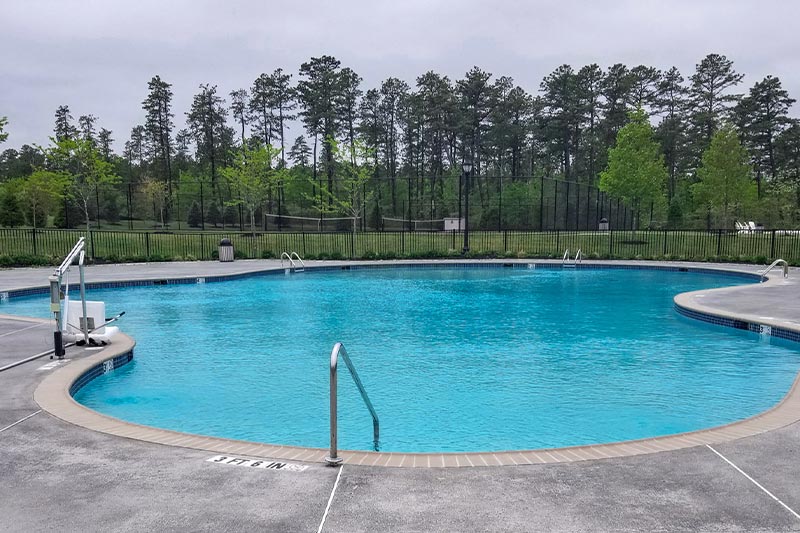 View of the outdoor pool and patio at Seacrest Pines with trees in the background on a cloudy day.