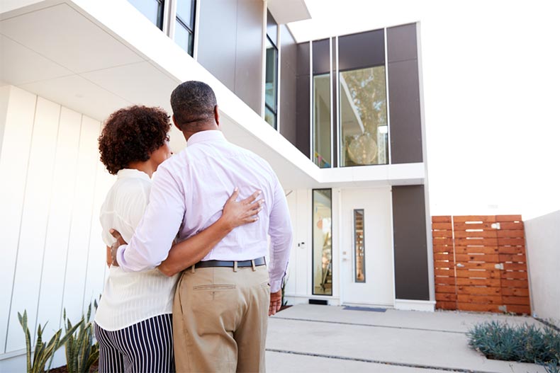 A back view of a retired couple standing outside their new modern home