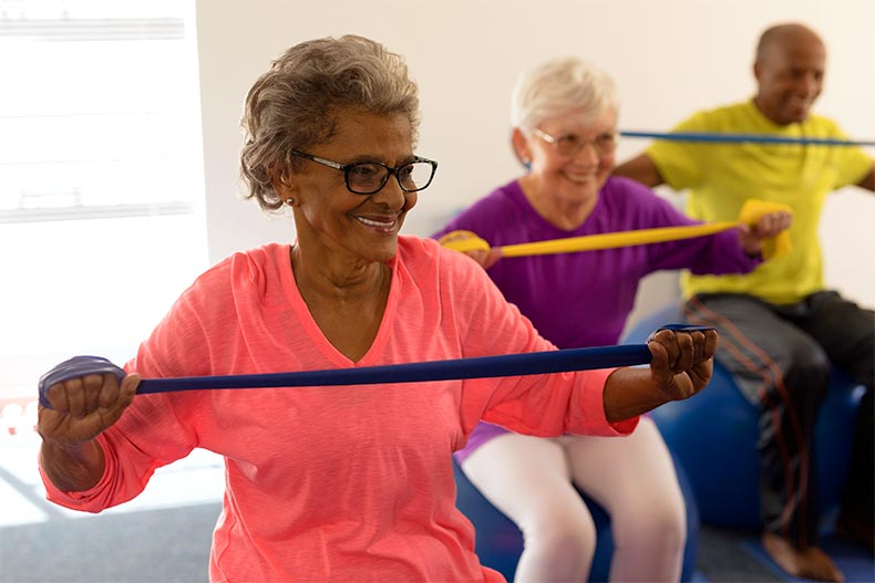 Two happy senior women and one man work out on exercise balls with resistance bands