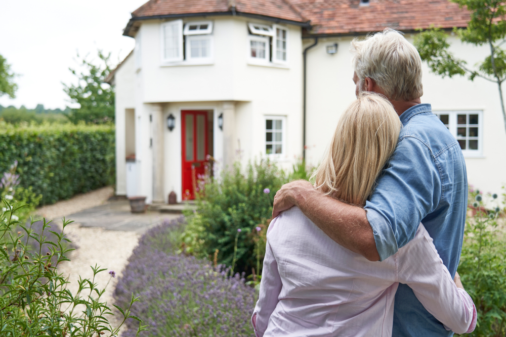 Rear view of a mature couple standing in a garden and looking at their dream home in the countryside
