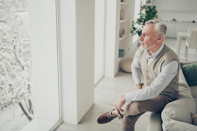 An older man looking out the window during the winter