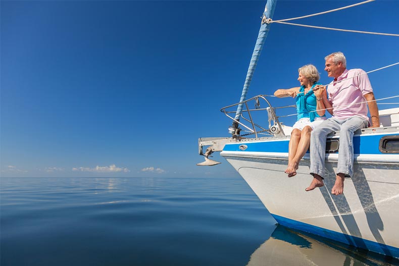 A happy senior couple sitting on the side of a sail boat on a calm blue sea
