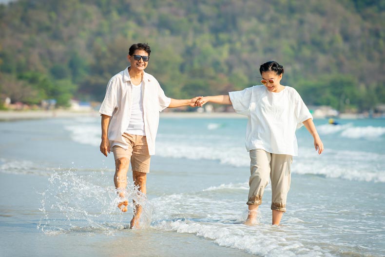 A snowbird couple holding hands and walking together on a beach