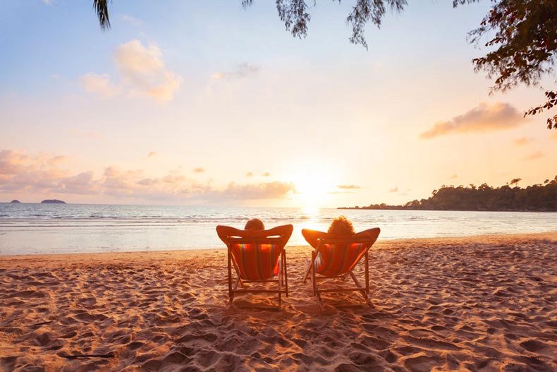 Silhouettes of a man and woman relaxing in lounge chairs beside the beach