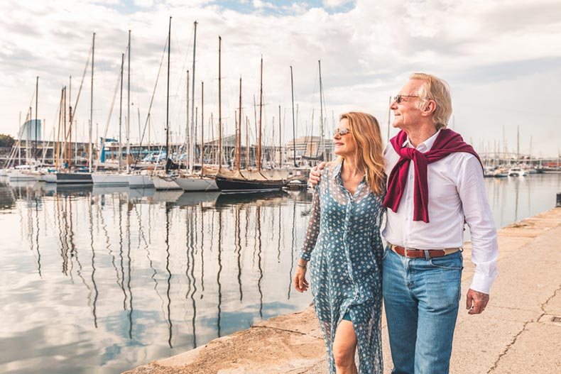 A snowbird couple walking beside a marina with boats on a sunny day