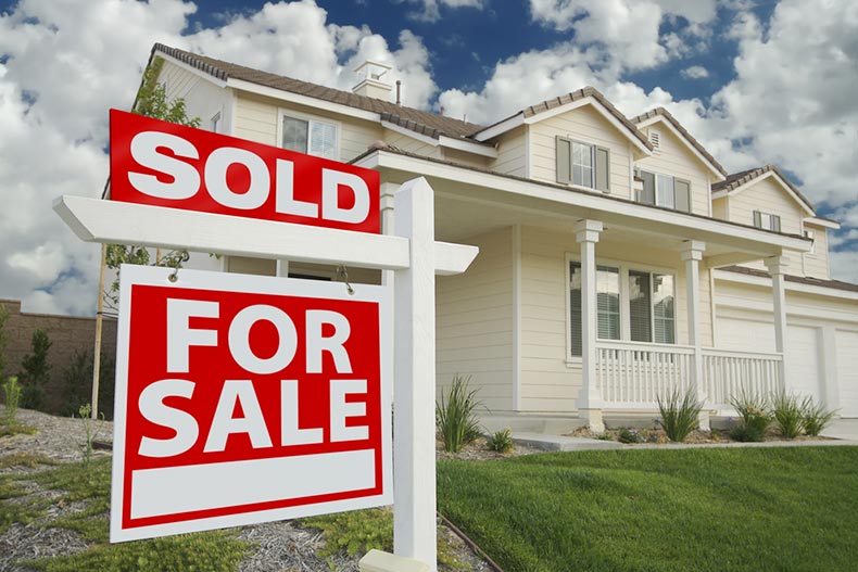 A large single-family home with a "For Sale" sign on the front lawn and a "Sold" sign above it