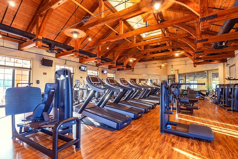 Rows of fitness equipment in a gym with hardwood flooring and exposed beam ceilings, located in the Solivita 55+ community of Kissimmee, Florida