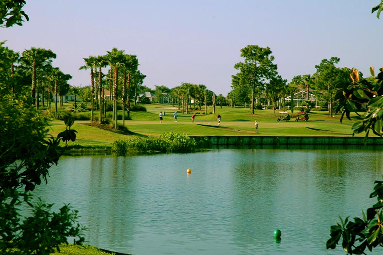 View of golfers playing from across a pond in Spruce Creek Country Club, located in Summerfield, Florida