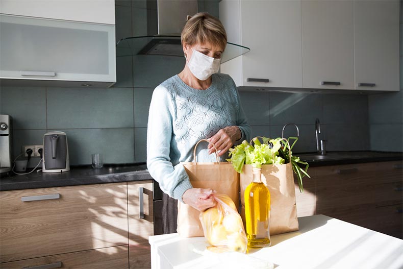 Seniors woman wearing a medical face mask while unpacking groceries