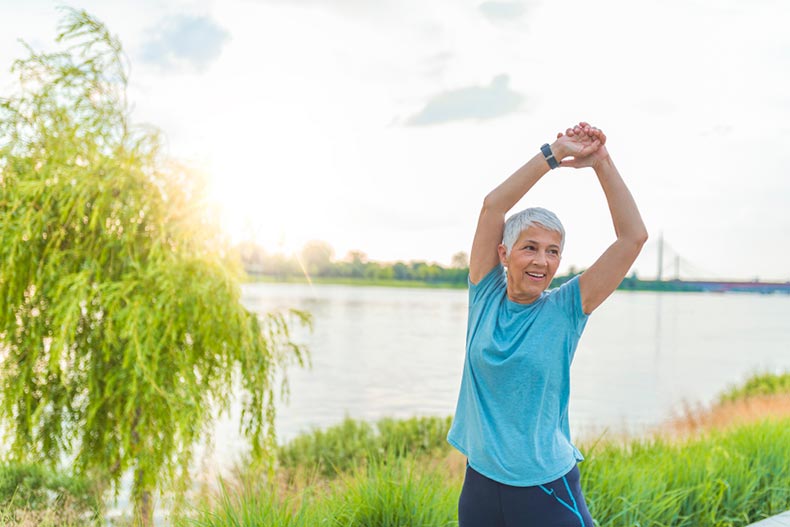 A mature woman stretching before a workout beside a lake in her 55+ community