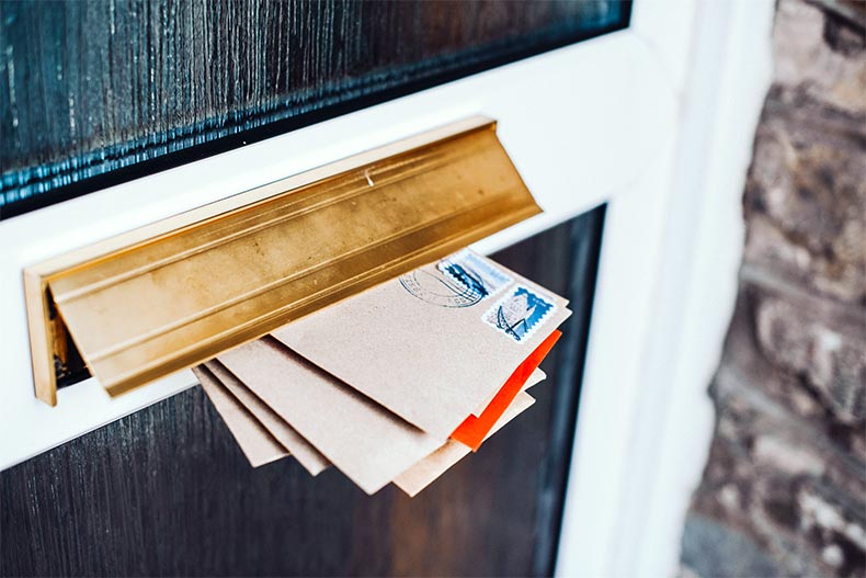 View of a mail slot stuffed with letters inside a dark brown wooden door